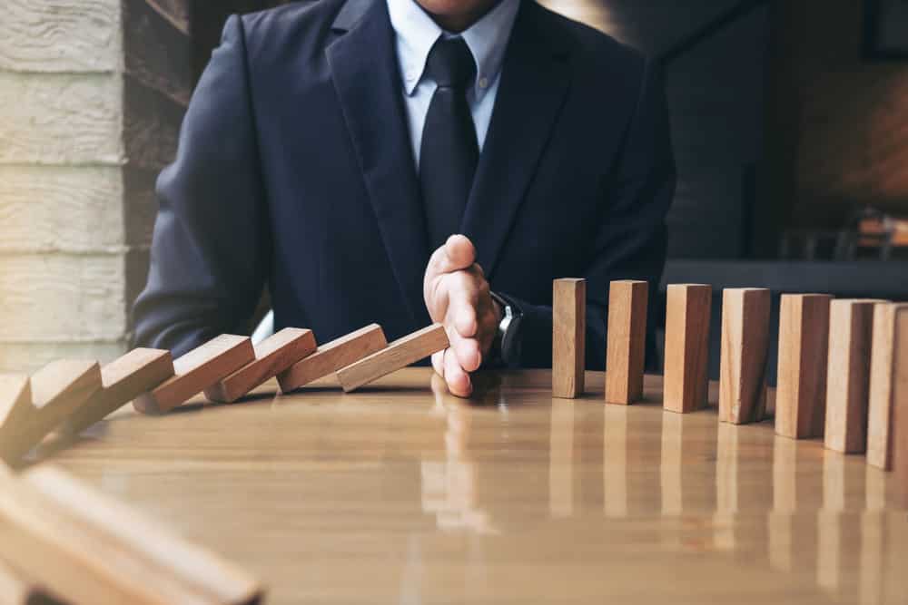 Close up of businessman hand Stopping Falling wooden Dominoes effect from continuous toppled or risk, strategy and successful intervention concept for business.